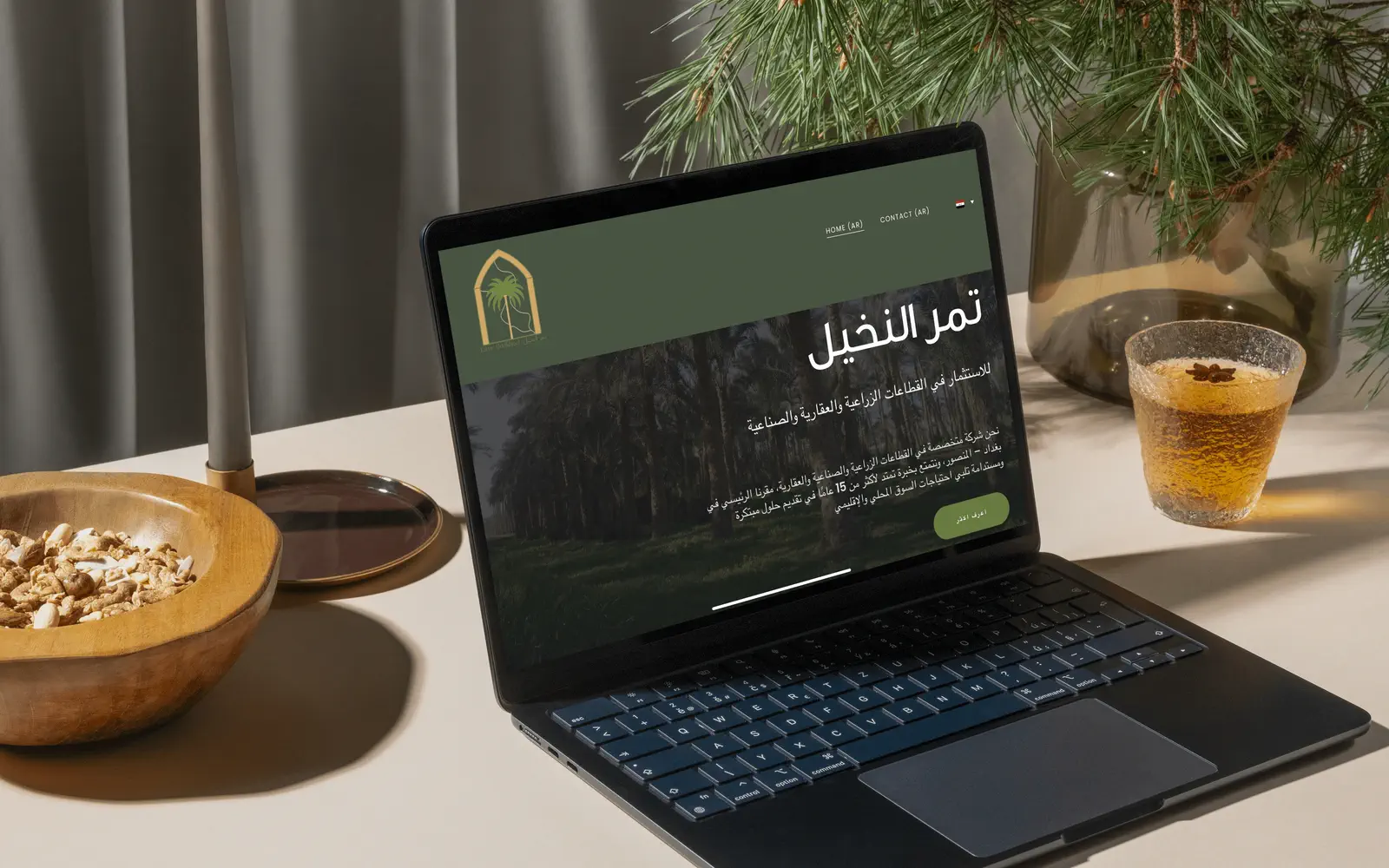The Tamr Alnakheel Arabic website open on a laptop beside dates and tea